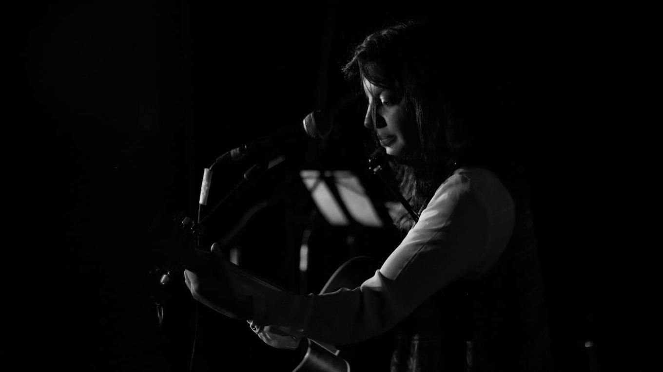 Foto blanco y negro de Esther en escenario con guitarra y delante de un microno, desde el lateral.